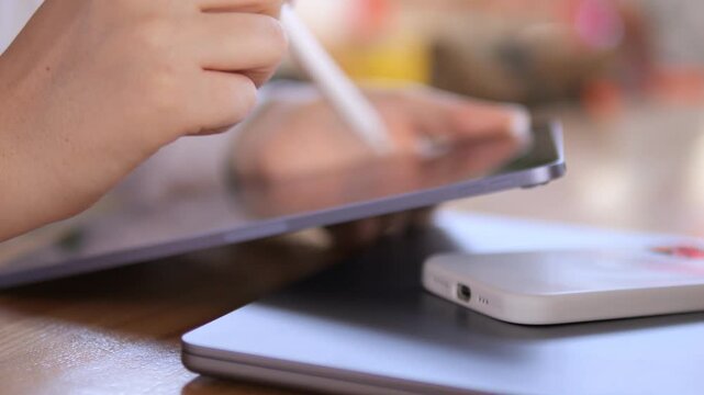 Person is writing on a tablet with a white pen. A cell phone is on the table next to the tablet
