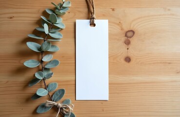 Blank bookmark mockup with jute string hangs on wooden surface. Natural green plant branch with leaves adorns empty card for notes sale tag. Simple, rustic design conveys natural, organic, handmade