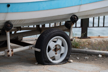 Deflated tire on a trailer platform carrying a small boat, parked outdoors on a gravel surface
