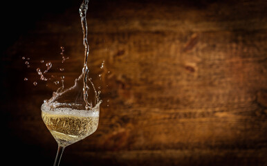 White sparkling wine being poured into a glass with splash and bubbles, set against a warm wooden background. Ideal for celebration visuals, bar menus, drink branding, or holiday designs.