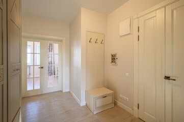 well-lit hallway features neutral tones, light wood floors, a glass-paneled double door, a closet, coat hooks and a bench with a small framed picture on the wall