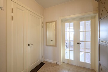 Bright hallway with white doors, a mirror, and tiled floors. Light colors create a clean, modern look