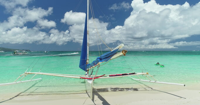 Turquoise tropical water gently lapping the shore of White Beach in Boracay, Philippines, with a traditional paraw sailboat resting on pristine sand under a vibrant blue sky