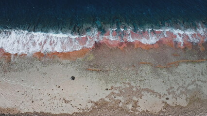 French Polynesia, Rangiroa island: Aerial view of ocean waves colorful shoreline crashing pink coral reef rocky beach, creating a beautiful natural spectacle. Drone top down static background © Goinyk