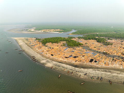 Aerial view of scattered dwellings nestled along the sandy shoreline, where the river meets the sea, contrasting with the lush green mangrove forest, Sundarban, Khulna Division, Bangladesh.