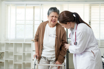 Fototapeta premium Doctor assisting elderly Asian woman who shows discomfort while using walker during rehabilitation session, highlighting pain and determination in recovery from joint problems