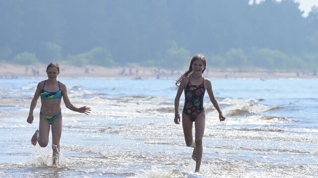 Two teenage girls running on water on a summer sea beach and having fun. Slow motion.