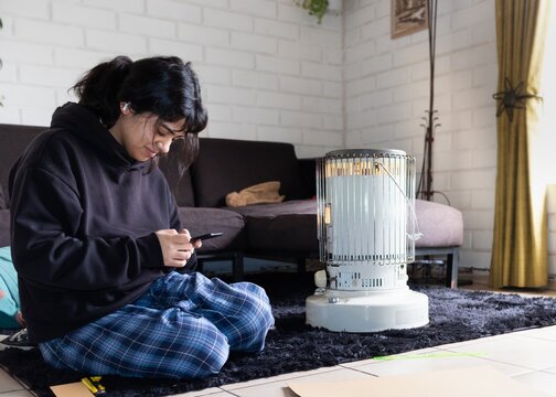 teenage girl sitting on the living room floor next to a kerosene stove heater
