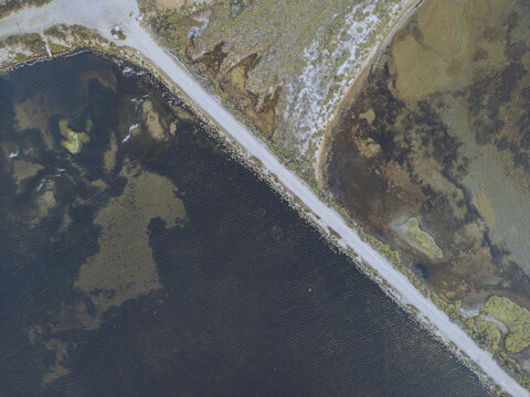 Aerial view of a narrow strip of land dividing the dark waters from the colorful salt marshes, Gruissan, Occitanie, France.