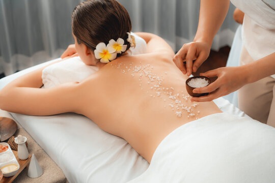 Woman customer having exfoliation treatment in luxury spa salon with warmth candle light ambient. Salt scrub beauty treatment in health spa body scrub. Quiescent - Powered by Adobe
