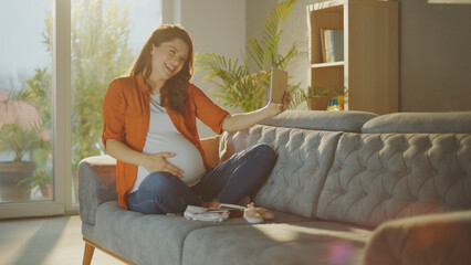 Pregnant woman using tablet and showing her belly during video call at home