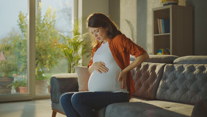 Pregnant woman experiencing back pain while sitting on sofa at home