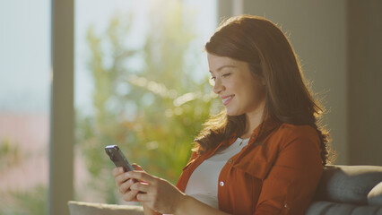 Pregnant woman relaxing on sofa using smartphone at home