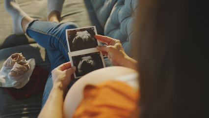 Pregnant woman relaxing on sofa holding ultrasound scan photos