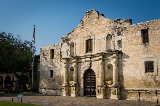 The Alamo Church San Antonio Texas historical landmark with USA flag waving in the background against a clear blue sky on a sunny day