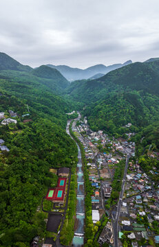 Aerial view of a town nestled in a valley between verdant mountains, with a river snaking through the heart of the landscape, Gora, Kanagawa, Japan.