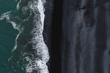 Reynisfjara's black volcanic sand meets the turquoise Atlantic Ocean, with white waves creating striking contrasts and dynamic textures in Iceland. © Aerial Film Studio