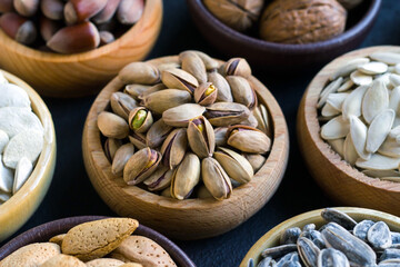 New harvest nuts in shells, designed on a black background in wooden bowls.Selected pistachio bowl