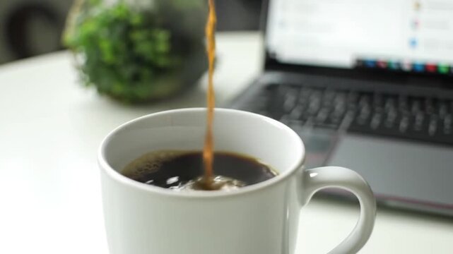 Aromatic Coffee Pour: A close-up shot captures the dynamic moment of coffee pouring into a pristine white mug, beside a laptop