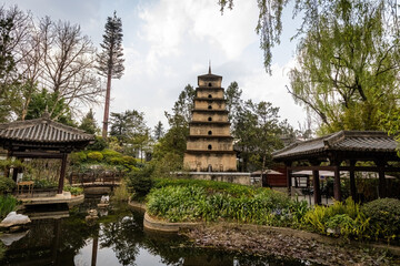 Ancient multi-tiered pagoda surrounded by lush greenery and traditional architecture at Yunnan Ethnics Village in Kunming, China