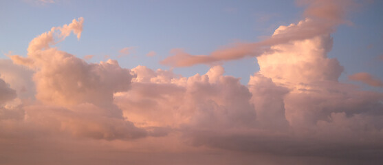 Towering clouds illuminated in warm orange and pink hues by the setting sun, standing against a soft gradient sky transitioning from blue to purple, creating a serene and dramatic evening atmosphere.