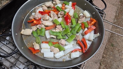 Traditional spanish paella with chicken and bell peppers on outdoor grill. Typical cuisine of Spain. Valencian cuisine. Stage of cooking paella. Ingredients for paella