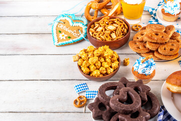 Oktoberfest festive food, with various snacks, sweets, desserts, pretzels, beer jelly, gingerbread cookies hearts, salted crackers, popcorn, jam donuts, cupcakes. Oktoberfest brunch menu background