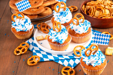 Oktoberfest cupcakes with salted pretzel, whipped cream on top and colorful sugar sprinkles, on white wooden background with Oktoberfest holiday decor, copy space