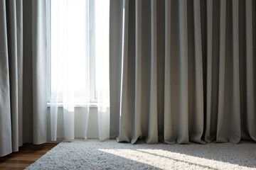 Elegant long beige blackout curtains hang gracefully from ceiling to floor in a cozy, sunlit bedroom, with soft morning light from window casting shadows on plush white carpet