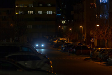 At nighttime, various cars are parked along the side of the road, creating an interesting scene illuminated by streetlights and moonlight