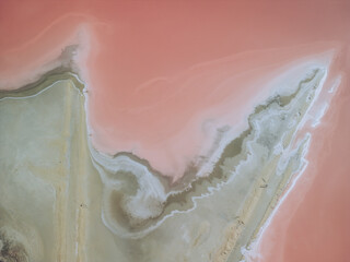 Aerial view of contrasting pink waters meet the earthy shore, swirling in patterns of white and beige, Route du Grau du Roi, Aigues-Mortes, Occitanie, France.
