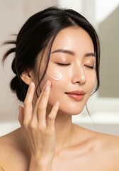 Naklejka premium Beautiful young Asian woman with perfect complexion applying moisturizing cream to her face. A serene moment of a daily skincare and beauty routine.