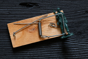 Plastic soldier in a mousetrap on a black wooden surface