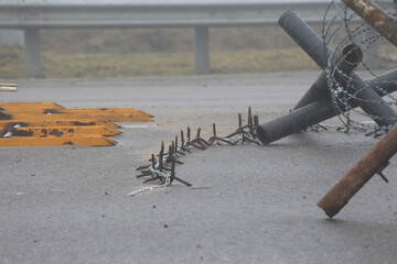 Close-up view of anti-vehicle and anti-tank barriers including metal spikes, chains, and barbed wire placed across a foggy road surface. Scene reflects conflict zone or security checkpoint defense.