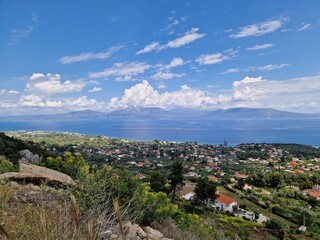 Breathtaking coastal village in Greece showcasing stunning seaside views, lush greenery, and vibrant rooftops under a bright blue sky with scattered clouds