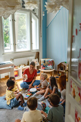 Teacher engaging a diverse group of preschool children in a fun indoor activity, sitting together in a circle and developing social and learning skills in a cozy kindergarten classroom