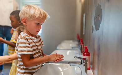 Children from diverse backgrounds washing hands with soap at preschool sinks, practicing good hygiene habits.