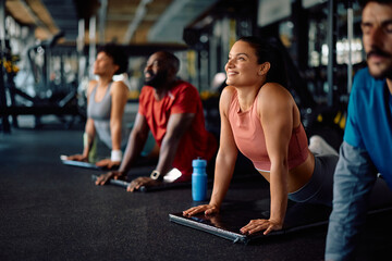 Happy athletic woman doing Sun Salutation exercise during group gym workout.