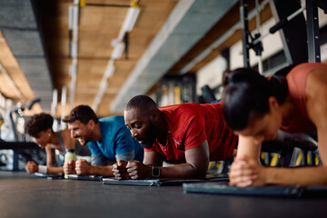 Group of athletes doing plank exercise while working out in gym.