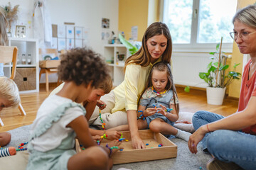 Two preschool teachers with children sitting on floor, engaging in collaborative early learning activity in bright classroom