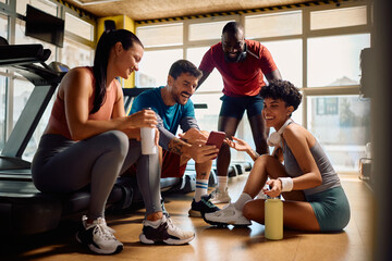 Happy athletic friends using smart phone during break in health club.