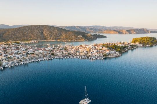 Aerial view of a Greek town nestles by the azure sea, a tapestry of sun-kissed rooftops and winding streets, with distant mountains, Ermioni, Argolis, Greece.