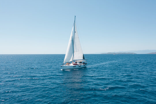 Aerial view of a sailboat gliding across the turquoise waters, sails billowing against the clear sky, a serene maritime scene, Ermioni, Argolis, Greece.