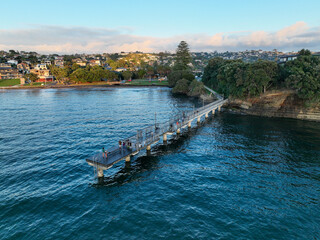 Aerial view of a long pier extending into the glistening water, contrasting with the lush green coastline, creating a serene coastal scene, Auckland, Auckland, New Zealand.