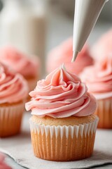 A baker decorates delicious vanilla cupcakes with soft pink buttercream frosting using a piping bag. The warm kitchen offers a comforting, inviting atmosphere