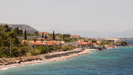 Coastal village in Greece showcases vibrant seaside cottages, lush greenery, and shimmering blue waters, inviting visitors to explore its tranquil charm under clear skies