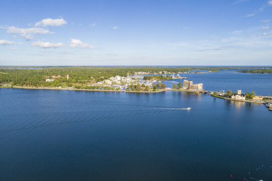 Aerial view of the shimmering blue waters embracing V&Atilde;&curren;stervik's coastline, where buildings nestle amidst verdant trees and a solitary boat glides across the water, Vastervik, Kalmar County, Sweden.