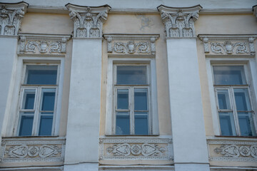 Windows with ornate stucco decorations and Corinthian-style columns on a historic building facade in Moscow, in soft beige and white tones