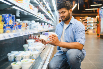 Indian man choosing yogurt in supermarket refrigerator dairy section