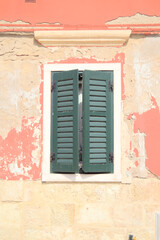 Rustic Venetian window with peeling wall and green shutters